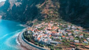 Stunning aerial view of a coastal town in Madeira, Portugal, with lush cliffs and turquoise sea.
