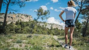 A woman explores a mountain trail surrounded by nature during a sunny day.